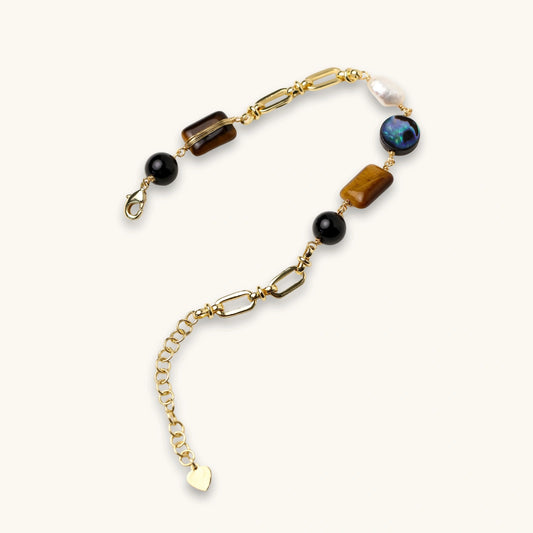 Gold chain bracelet with tiger's eye, obsidian, pearl, and iridescent abalone stones on cream background.